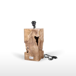 Puede incluir: Una lámpara de mesa de madera con un acabado de madera natural y una pantalla negra. La base de la lámpara está hecha de una sola pieza de madera con una forma orgánica única. La lámpara está cableada con un cable y un enchufe negros.