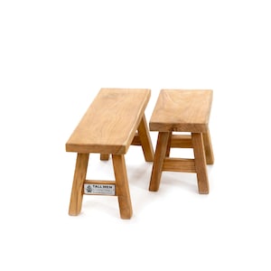 Könnte beinhalten: Zwei Holzbänke, eine größer als die andere, aus Naturholz mit hellbrauner Oberfläche. Die größere Bank hat ein Etikett auf der Unterseite mit der Aufschrift "Tall Men Standing".