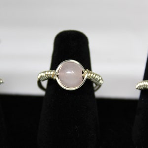 May include: A silver wire wrapped ring with a pale pink oval gemstone.