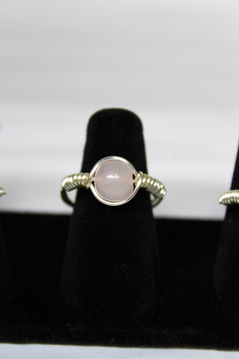 May include: A silver wire wrapped ring with a pale pink oval gemstone.