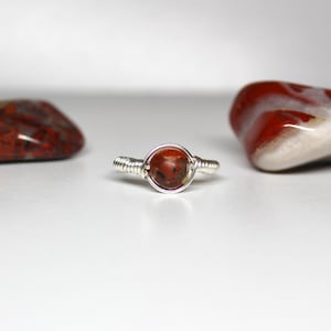 May include: A silver wire wrapped ring with a red and white jasper stone.