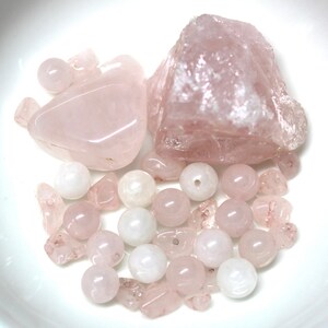 May include: A collection of pink rose quartz crystals and beads. The crystals are in various shapes and sizes, including a large, irregular shaped crystal. The beads are round and smooth.