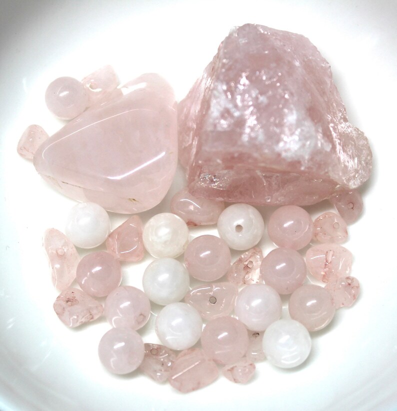 May include: A collection of pink rose quartz crystals and beads. The crystals are in various shapes and sizes, including a large, irregular shaped crystal. The beads are round and smooth.