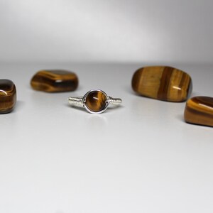May include: A silver wire wrapped ring with a round tiger's eye gemstone. The ring is surrounded by four tiger's eye stones.