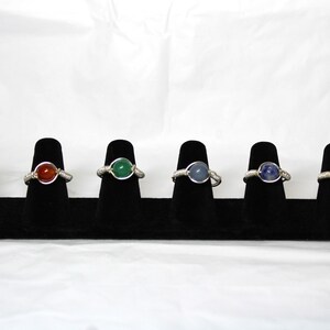 May include: Six wire-wrapped rings with different colored gemstones. The rings are displayed on a black velvet ring display stand.