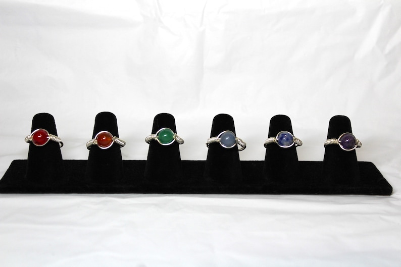 May include: Six wire-wrapped rings with different colored gemstones. The rings are displayed on a black velvet ring display stand.