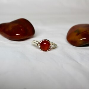 May include: A silver wire wrapped ring with a round, orange carnelian gemstone.