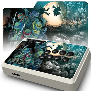 May include: A white arcade stick with a black joystick and eight black buttons. The stick is decorated with a Teenage Mutant Ninja Turtles graphic featuring the four turtles in a fighting pose against a cityscape background.