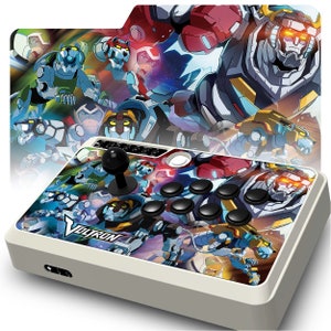May include: A white arcade joystick with a Voltron design. The joystick features a black ball top and eight black buttons. The design includes images of the Voltron robot and its five lions.