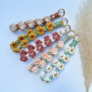 May include: Five colorful crocheted keychains with flower designs. Each keychain features a different color combination and flower pattern. The keychains are made with a variety of yarn colors, including green, white, brown, and pink.