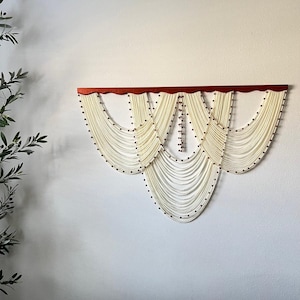 May include: A white beaded wall hanging with a red wooden top. The beads are arranged in a cascading pattern, creating a decorative and elegant look.