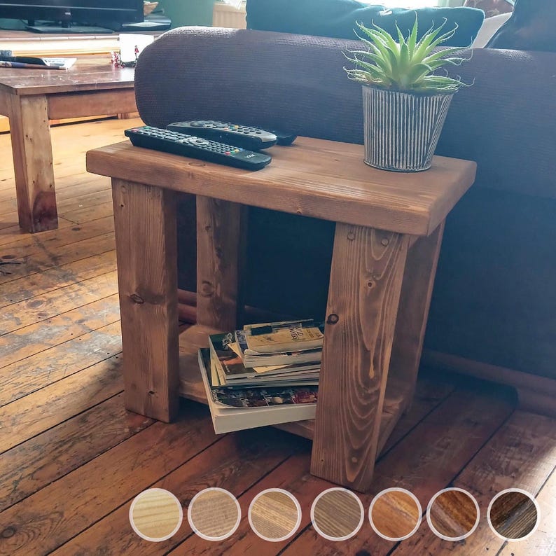 May include: A rustic wooden end table with a natural brown finish. The table has a shelf for storage and is ideal for a living room or bedroom. The table is next to a brown sofa and has a potted plant on top.