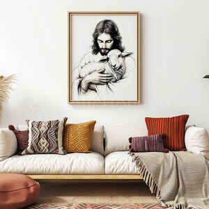 May include: A framed black and white art print depicts a figure holding a lamb. The artwork is displayed above a white sofa with decorative pillows in shades of brown, orange, and burgundy. A neutral-toned throw blanket and a floor cushion complete the scene.