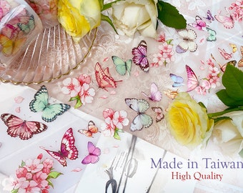 May include: A roll of decorative washi tape featuring a delicate design of butterflies and pink flowers. The tape is on a white background with a text overlay that reads "Made in Taiwan High Quality".