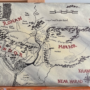 May include: A hand-drawn map of Middle-earth from The Lord of the Rings, featuring the regions of Rohan, Gondor, Mordor, and Rhun. The map is drawn in black ink on a beige canvas background.