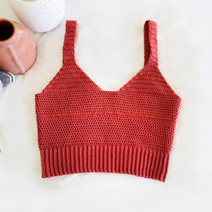 May include: A red crocheted tank top with thin straps. The top has a V-neck and a ribbed hem.