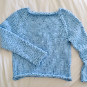 May include: A light blue knitted sweater with long sleeves and a round neckline.