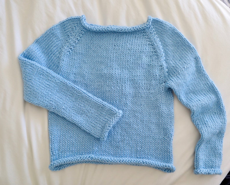 May include: A light blue knitted sweater with long sleeves and a round neckline.