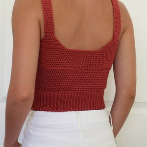 May include: A rust-colored crochet tank top with a square neckline and thin straps. The top is cropped and has a ribbed hem.