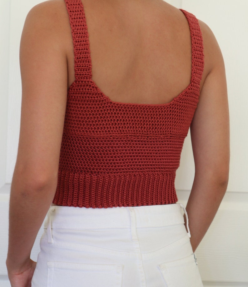 May include: A rust-colored crochet tank top with a square neckline and thin straps. The top is cropped and has a ribbed hem.