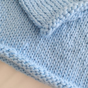 May include: A close-up of a light blue knitted blanket with a chunky knit texture.