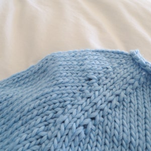 May include: Close-up of a light blue knitted sweater with a chunky knit texture.
