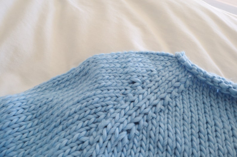 May include: Close-up of a light blue knitted sweater with a chunky knit texture.