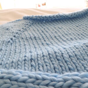 May include: A close-up of a light blue knitted blanket with a textured weave. The blanket is soft and fluffy, and it appears to be made of a chunky yarn.