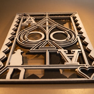 Pode incluir: Um recorte de madeira do naipe Ás de Espadas. O cartão é em camadas e apresenta um design detalhado do símbolo do naipe. O cartão é em preto e branco.