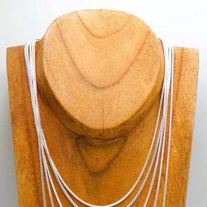 May include: A silver chain necklace on a wooden display stand. The chain is layered in a graduated pattern, with the longest chain at the bottom and the shortest chain at the top.