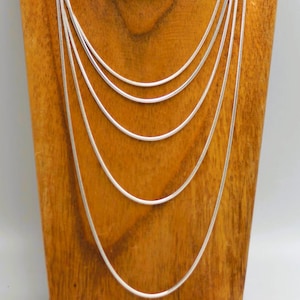 May include: A set of seven silver snake chains of varying lengths displayed on a wooden stand.