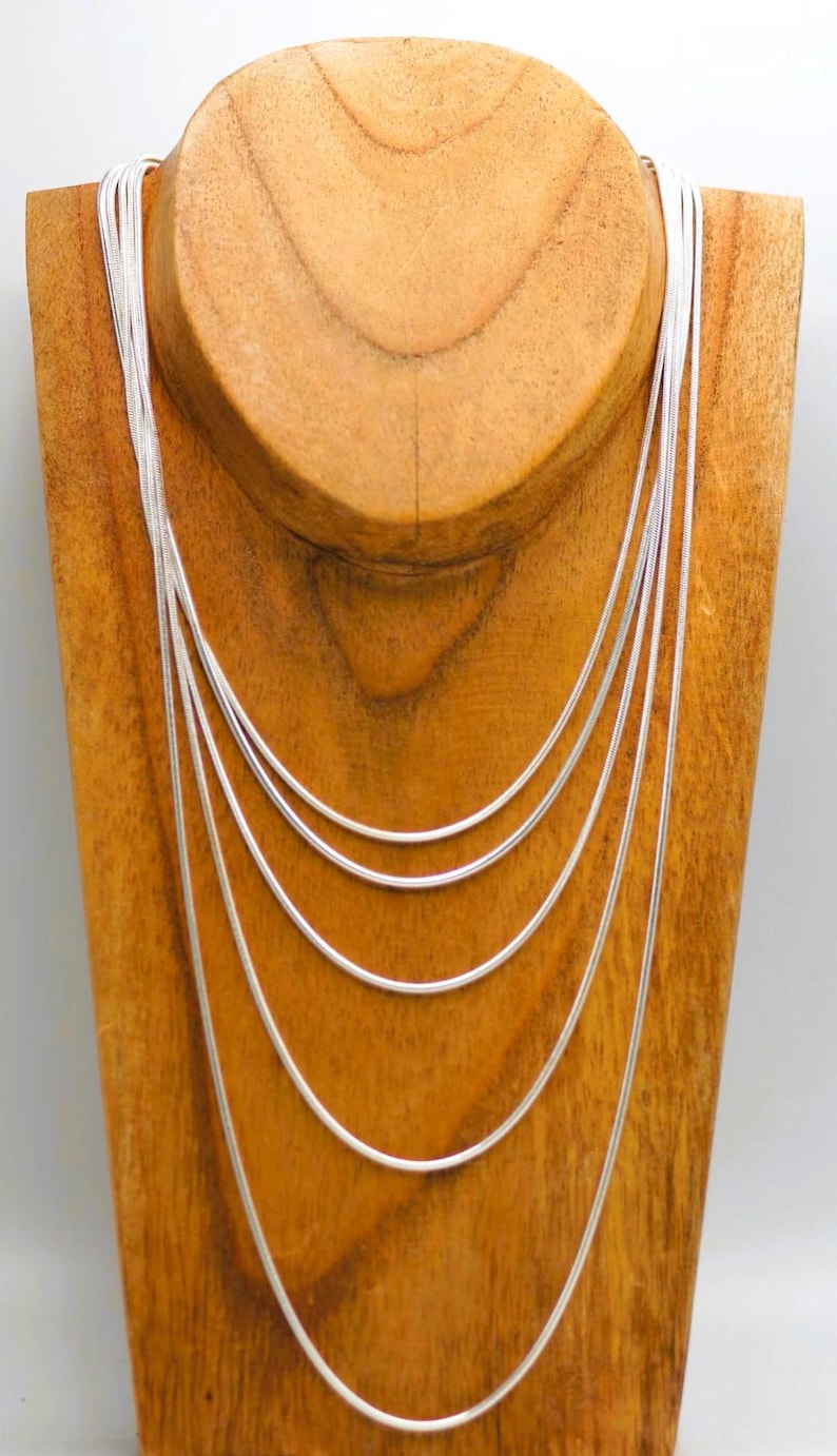 May include: A silver chain necklace on a wooden display stand. The chain is layered in a graduated pattern, with the longest chain at the bottom and the shortest chain at the top.