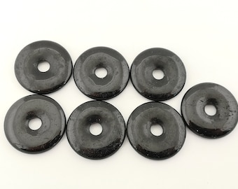 Könnte beinhalten: Sieben schwarze Obsidian-Donut-Perlen mit einem Loch in der Mitte. Die Perlen sind glatt und poliert.