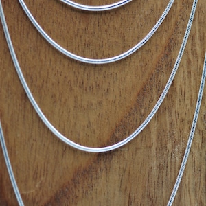 May include: Five silver snake chains of varying lengths, displayed on a wooden surface.