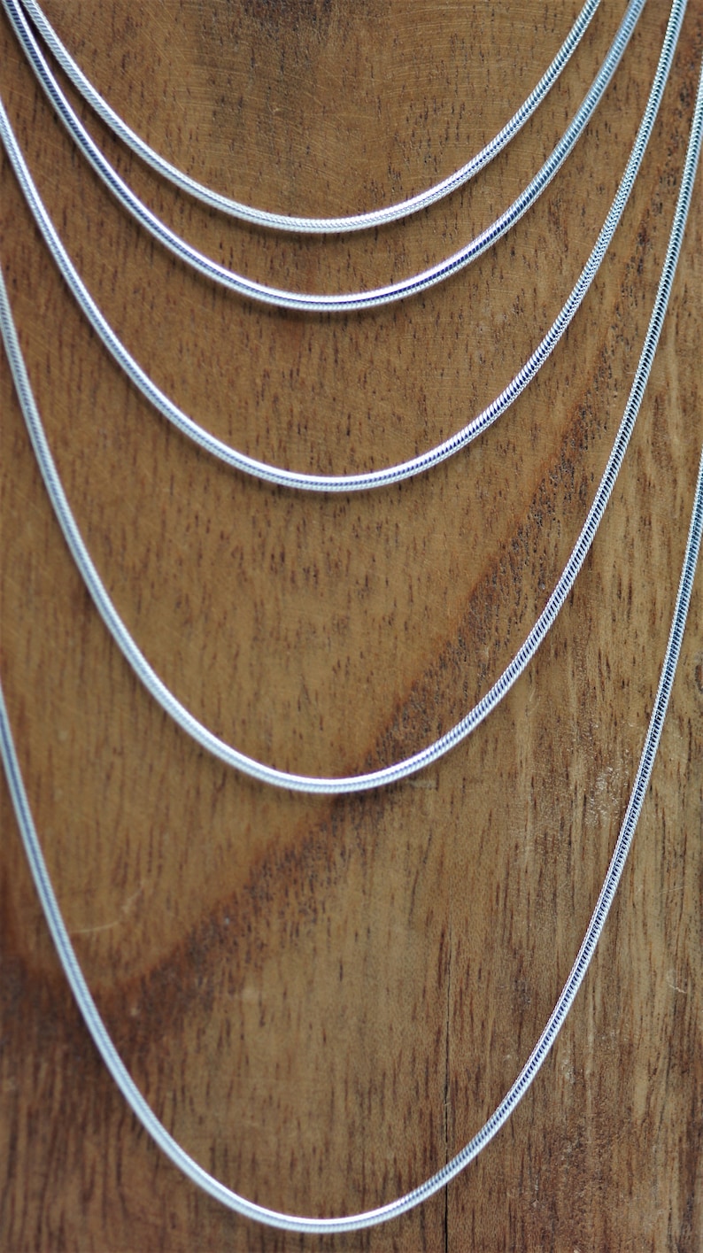 May include: Five silver snake chains of varying lengths, displayed on a wooden surface.