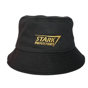May include: Black bucket hat with the gold text "STARK INDUSTRIES". The hat has a rounded crown and a downward-sloping brim. The hat is made of a soft material and is suitable for casual wear.