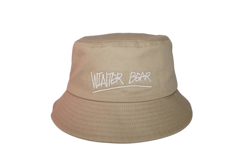 May include: A beige bucket hat with the words "Winter Bear" embroidered in white on the front.
