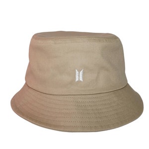May include: A beige bucket hat with a white embroidered logo of a stylized "B" with wings.