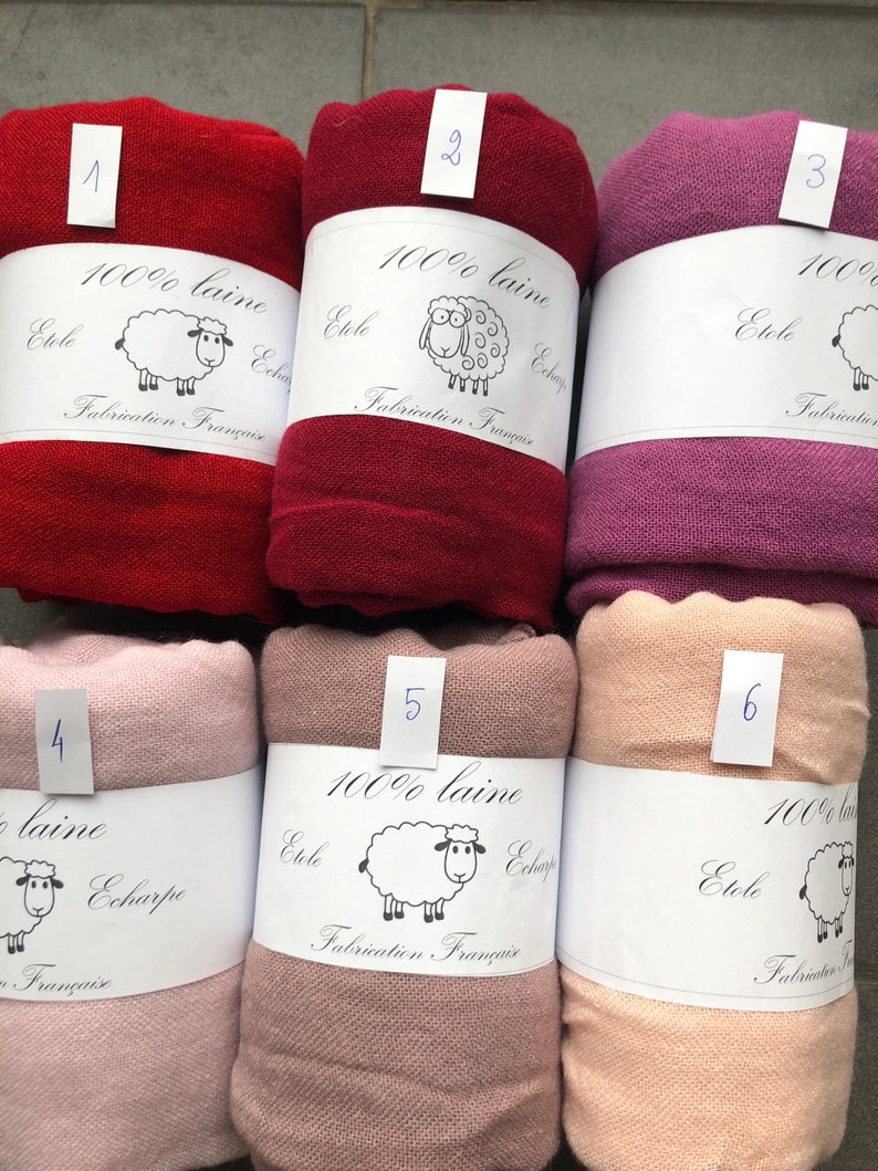 Pode incluir: Seis cachec&oacute;is de l&atilde; enrolados em v&aacute;rias cores, incluindo vermelho, bord&ocirc; e rosa. Cada cachecol &eacute; rotulado com um n&uacute;mero e uma faixa branca com uma ilustra&ccedil;&atilde;o de ovelha e o texto "100% laine, Etole, Echarpe, Fabrication Fran&ccedil;aise."