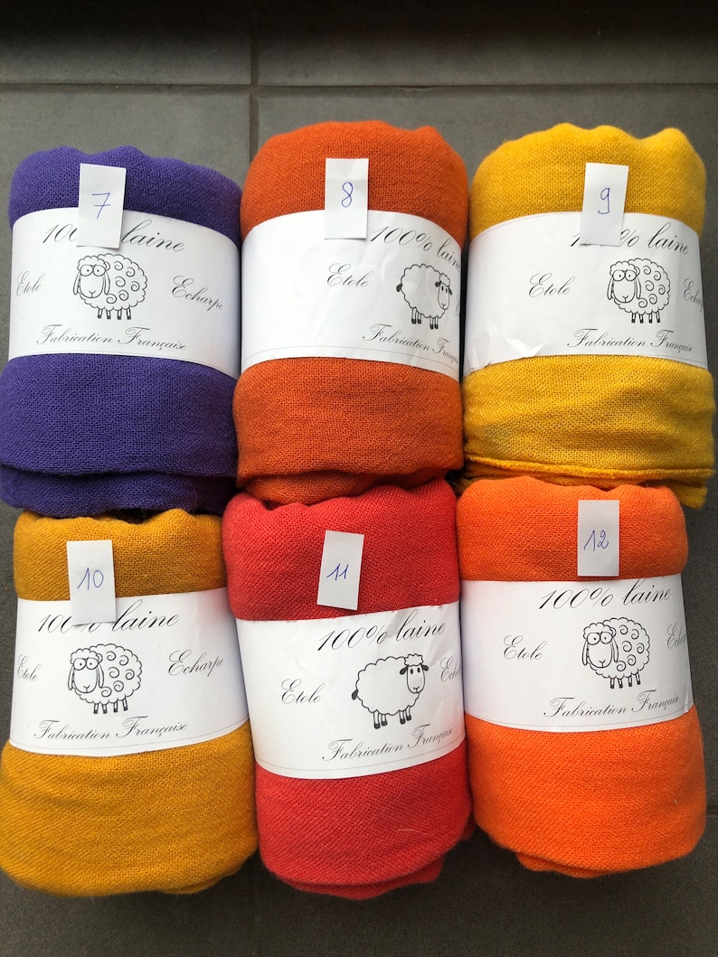 Pode incluir: Seis echarpes de l&atilde; enroladas em v&aacute;rias cores: roxo, laranja, amarelo e vermelho. Cada echarpe &eacute; rotulada com um n&uacute;mero e o texto "100% laine Etole Echarpe Fabrication Fran&ccedil;aise" com uma ilustra&ccedil;&atilde;o de ovelha.
