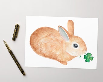 May include: A watercolor painting of a brown rabbit with a green four-leaf clover in its mouth.