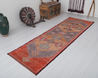 Puede incluir: Una alfombra larga y estrecha con un diseño persa tradicional. La alfombra es principalmente naranja con un patrón geométrico en tonos de azul, gris y beige.