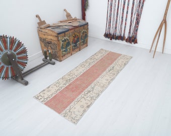Puede incluir: Una alfombra de pasillo vintage con fondo crema y una amplia franja horizontal de color melocotón en el centro. La alfombra tiene un aspecto descolorido y desgastado y patrones florales intrincados.