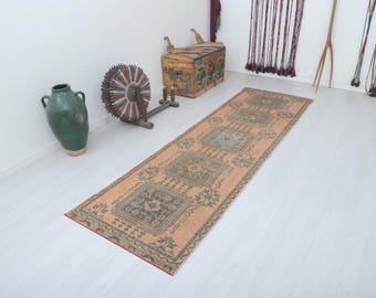 Op de afbeelding: Een vintage loper met een perzikkleurige achtergrond en een veelkleurig geometrisch patroon. De loper heeft een franje rand en is gemaakt van wol.