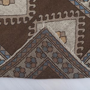 Puede incluir: Primer plano de una alfombra estampada marr&oacute;n y beige con un dise&ntilde;o geom&eacute;trico. La alfombra presenta un patr&oacute;n repetitivo de cuadrados y motivos florales en tonos marrones, beiges y azules. El borde de la alfombra tiene un borde decorativo.