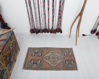 May include: A small, rectangular rug with a traditional Persian design. The rug has a light pink background with intricate patterns in shades of brown, cream, and blue.