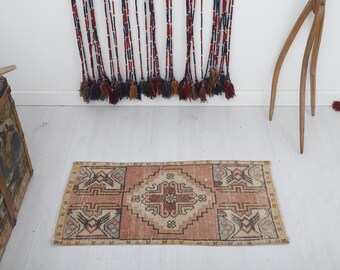 May include: A small, rectangular rug with a traditional Persian design. The rug is in shades of beige, pink, and brown. It has a fringe border.