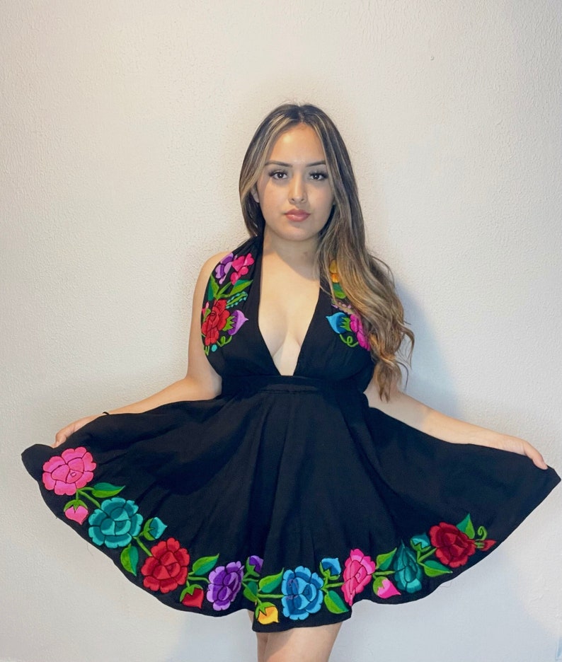 May include: A black sleeveless dress with a plunging neckline and a floral embroidery design. The embroidery features colorful flowers in shades of pink, red, blue, green, and yellow.