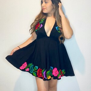 May include: A black sleeveless dress with a plunging neckline and a floral embroidery design around the hem. The embroidery features colorful flowers in shades of pink, red, green, blue, and yellow.