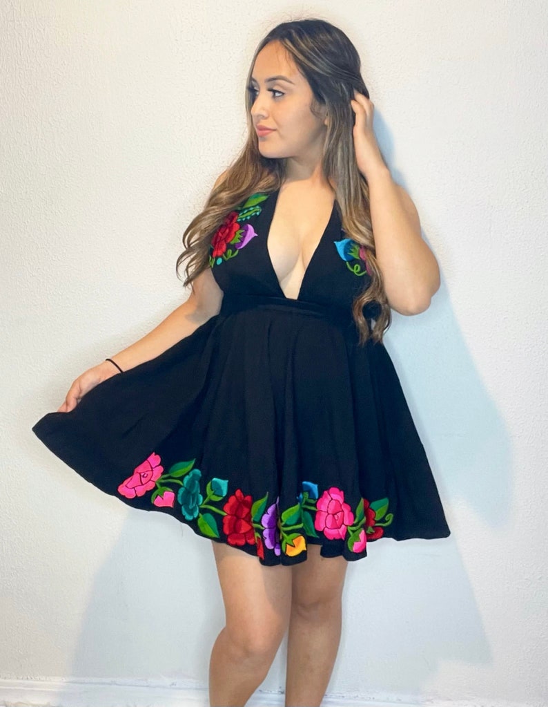 May include: A black sleeveless dress with a plunging neckline and a floral embroidery design around the hem. The embroidery features colorful flowers in shades of pink, red, green, blue, and yellow.